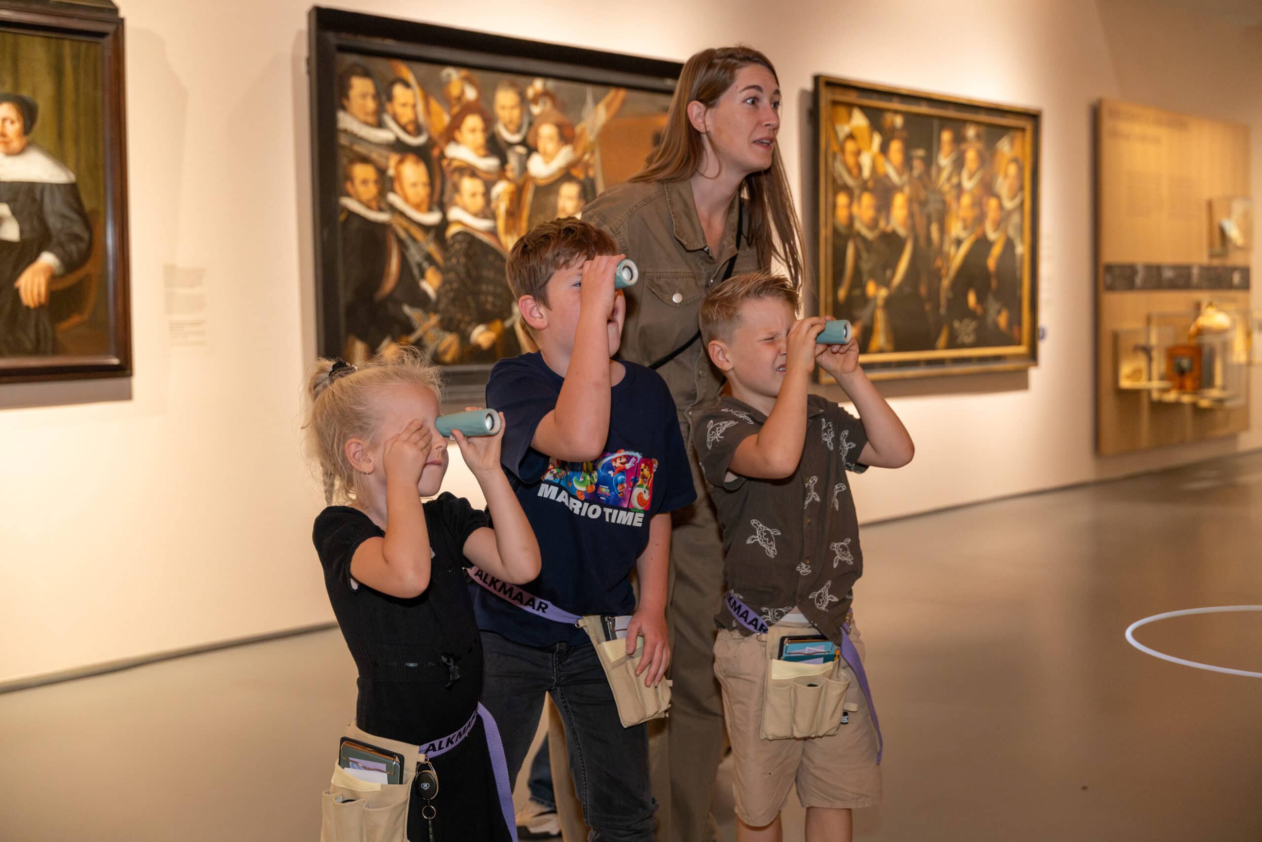 drie kinderen staan naar kunst te kijken met een verrekijker. hun moeder staat achter hen en kijkt ook.